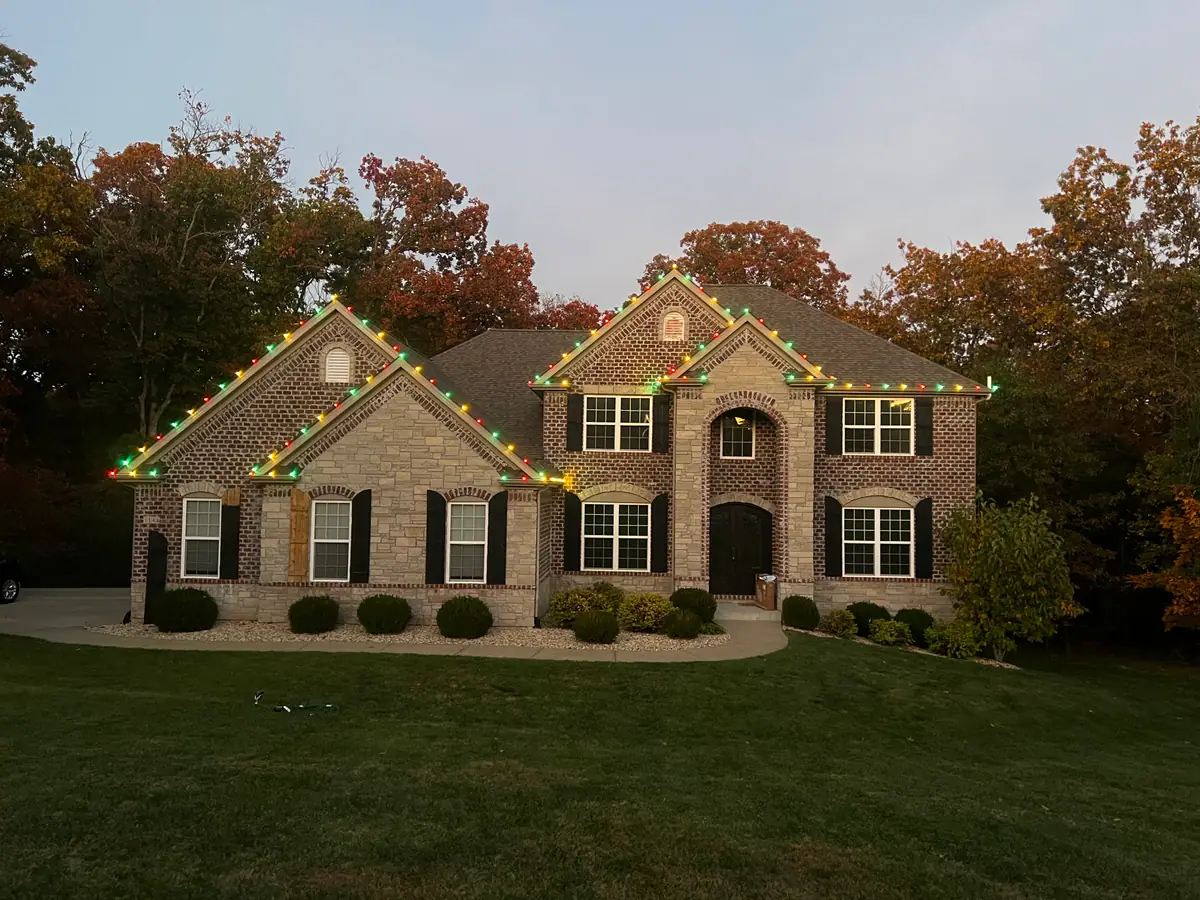 A brick two-story at dusk with colored C9 lights following every roofline